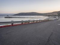 an empty highway with cars passing by and the water running parallel to each other with the sun setting behind