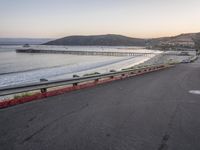 an empty highway with cars passing by and the water running parallel to each other with the sun setting behind