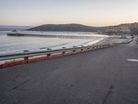 an empty highway with cars passing by and the water running parallel to each other with the sun setting behind