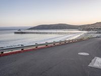 an empty highway with cars passing by and the water running parallel to each other with the sun setting behind