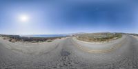 fisheye lens view of highway by the ocean with mountains and sun in background at the seaside