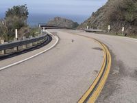 a motorcycle is driving down an empty winding road on a cliff side overlooking the ocean