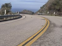 a motorcycle is driving down an empty winding road on a cliff side overlooking the ocean