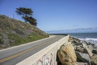 the road is next to a rocky cliff with the sea and the sky behind it