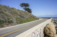 the road is next to a rocky cliff with the sea and the sky behind it