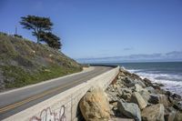 the road is next to a rocky cliff with the sea and the sky behind it