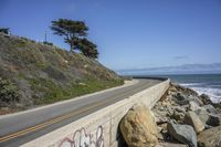 the road is next to a rocky cliff with the sea and the sky behind it