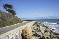 the road is next to a rocky cliff with the sea and the sky behind it