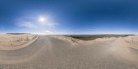 a 360 view of the highway with trees, sand and hills in the background, with sun