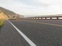 a bike is traveling along the road to a rocky beach side cliff area below it