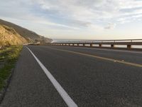 a bike is traveling along the road to a rocky beach side cliff area below it