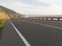 a bike is traveling along the road to a rocky beach side cliff area below it