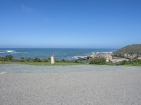 a fire hydrant on a grassy hillside near a ocean bank with surf and rocks