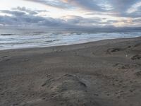 a beach and sand hill with some very nice ocean waves in the distance, and people walking in the foreground