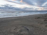 a beach and sand hill with some very nice ocean waves in the distance, and people walking in the foreground