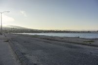 empty street along the edge of a body of water with mountains in the distance behind it