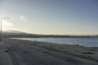 empty street along the edge of a body of water with mountains in the distance behind it