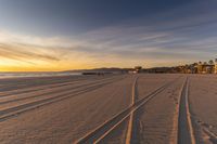 two tracks going up the sand towards the ocean at dusk with a resort in the distance