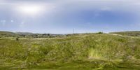 a wide shot of a grassy hill with some clouds in the sky and mountains behind it