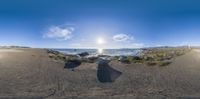 a fish eye view of the beach and the sun rising behind a rock in front of some water