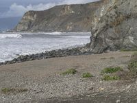 there is a man sitting on the sand near the ocean looking out at the beach