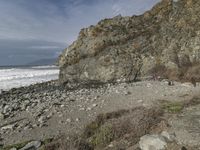 two people walking near the ocean by the rocky coastline and the cliffs in front are covered with large, blue rocks