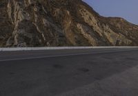 an empty highway with steep mountains in the back ground and a single car parked on it