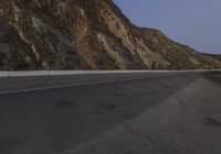 an empty highway with steep mountains in the back ground and a single car parked on it