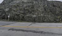 a man is standing on the side of a road near a hill of rocks with one standing on a sign