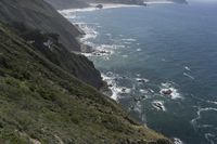 a man walking along a path beside the ocean in a scenic landscape area with a steep cliff to one side