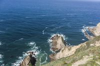 a man walking along a path beside the ocean in a scenic landscape area with a steep cliff to one side