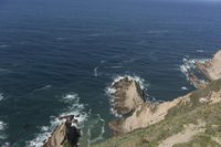 a man walking along a path beside the ocean in a scenic landscape area with a steep cliff to one side