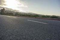 a skateboarder riding his board on an empty asphalted road with mountains in the background