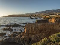 a grassy field by the shore and a cliff with rocks in the ocean in the background