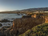 a grassy field by the shore and a cliff with rocks in the ocean in the background