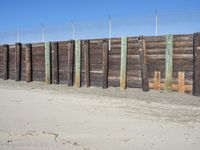 a fence of wood and posts on a sand area with the blue sky in the background