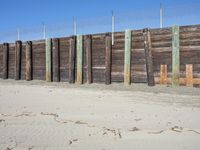 a fence of wood and posts on a sand area with the blue sky in the background