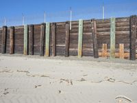 a fence of wood and posts on a sand area with the blue sky in the background