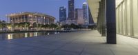 the walkway at the park leads to a lake and buildings in the background as evening falls