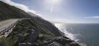 the road is winding and passing by the ocean with rocks below and trees growing on each side