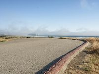 a sidewalk with a curb that runs alongside the beach and ocean, which is partly wet, the sun shines