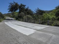 a road next to some trees and a fence with dirt path through it with a motorcycle parked at the end of it