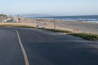 an empty road near a beach and waves as well as cars on the sand and houses on the beach