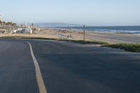 an empty road near a beach and waves as well as cars on the sand and houses on the beach