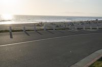 an empty road near a beach and waves as well as cars on the sand and houses on the beach