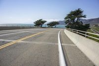 the view down a highway to the ocean from the top of a bridge with a line of yellow stripe in the center