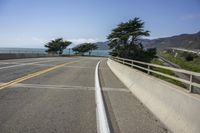 the view down a highway to the ocean from the top of a bridge with a line of yellow stripe in the center