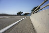 a road near the ocean has a cement barrier and tree lined street side in the foreground