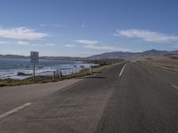 a highway on an ocean side with mountains in the background and a sign in foreground