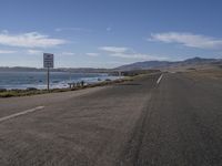 a highway on an ocean side with mountains in the background and a sign in foreground